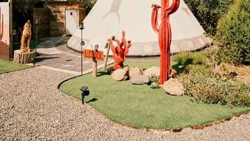 A tipi with a grassy area in front, a red sculpture, and a stone structure.
