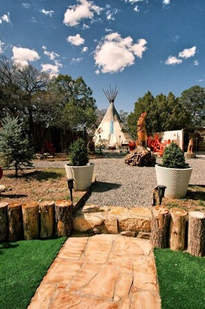 A traditional tipi surrounded by potted plants and a stone pathway.