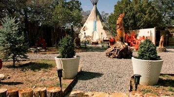 A traditional tipi surrounded by potted plants and a stone pathway.