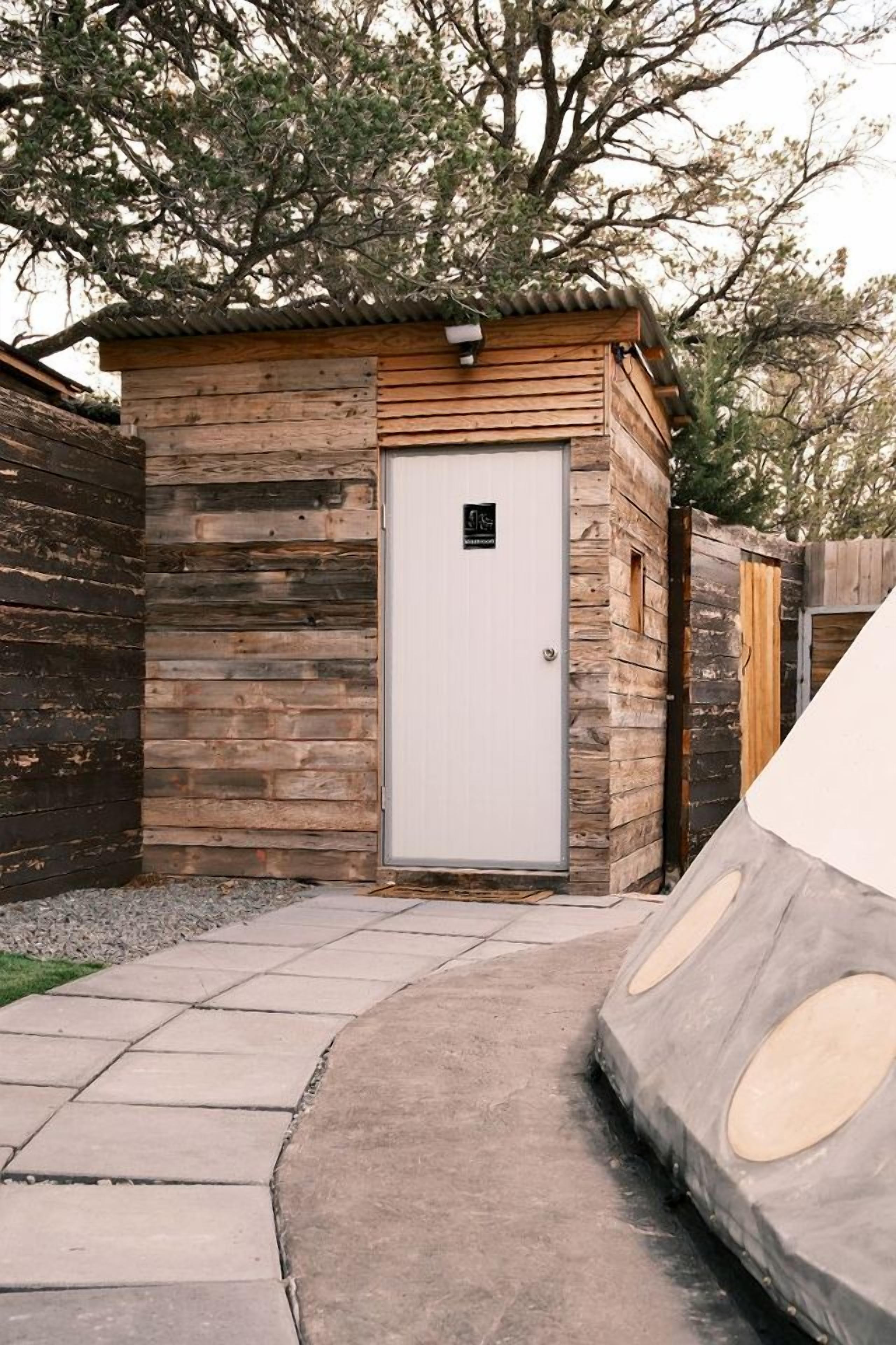 Una cabaña de madera con puerta blanca, un pequeño porche y un camino de hormigón que la conduce.