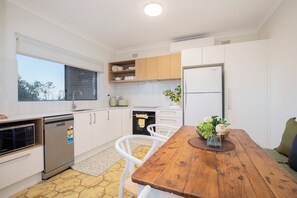 A modern kitchen with white cabinetry, a built-in oven, a dishwasher, and a refrigerator. - Tide and Stillness Idyllic Garden Escape by the Sea (Macmasters Beach)