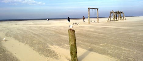 A sandy beach with a wooden post, swings, and a swing set.