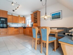 A kitchen with wooden cabinets, a dining table with chairs, and a hanging light fixture. - Holiday Apartment With 2 Bedrooms (St. Peter-Ording)