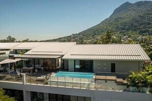A modern building with a swimming pool, flat roof, and a view of a mountain. - Luxury Penthouse with Private Pool (Grande Riviere Noire)