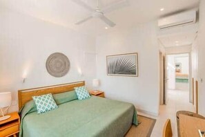 A bedroom with a bed, bedside tables, a ceiling fan, and a door leading to another room. - Luxury Penthouse with Private Pool (Grande Riviere Noire)
