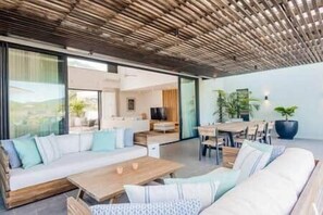 A modern living room with a wooden ceiling, a sofa set, a coffee table, and a dining area with a table and chairs. - Luxury Penthouse with Private Pool (Grande Riviere Noire)