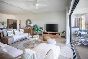 Ein modernes Wohnzimmer mit einer Couch, einem Fernseher und einem Balkon mit Pool.