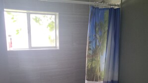 Un baño con inodoro, ducha con cortina, ventana y suelo de baldosas.