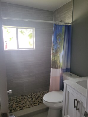 Une salle de bain avec des toilettes, une douche avec un rideau, une fenêtre et un sol carrelé.