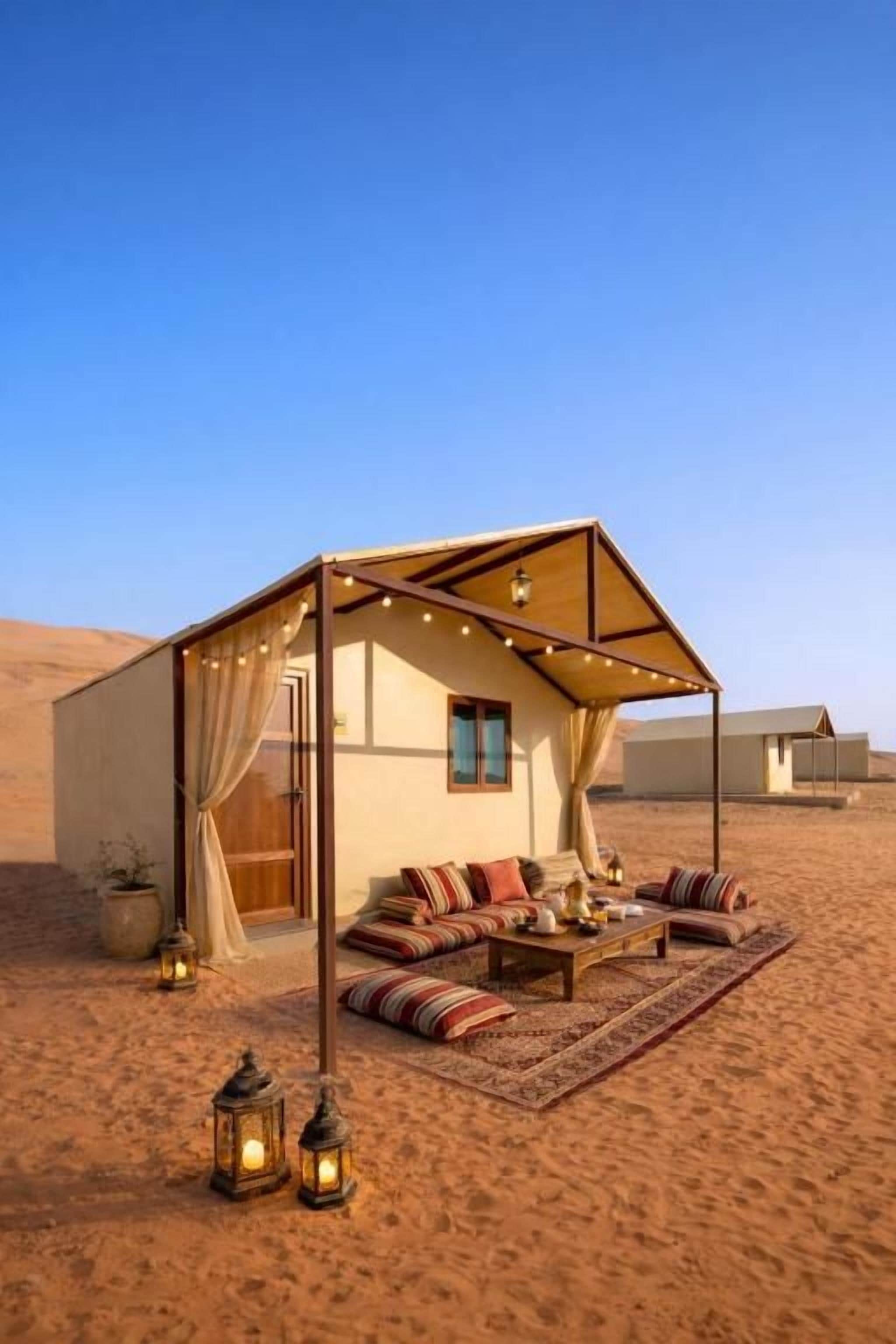 A desert tent with a sofa and a table, surrounded by sand.