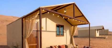 A desert tent with a sofa and a table, surrounded by sand.