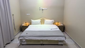 Un lit bien fait, avec une couette blanche et une parure rayée, deux tables de chevet avec des lampes, une prise de courant murale et une prise électrique.