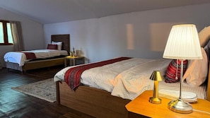 Ein Hotelzimmer mit zwei Betten, Holzboden, einem Nachttisch mit Lampe und einem Fenster mit Vorhängen.
