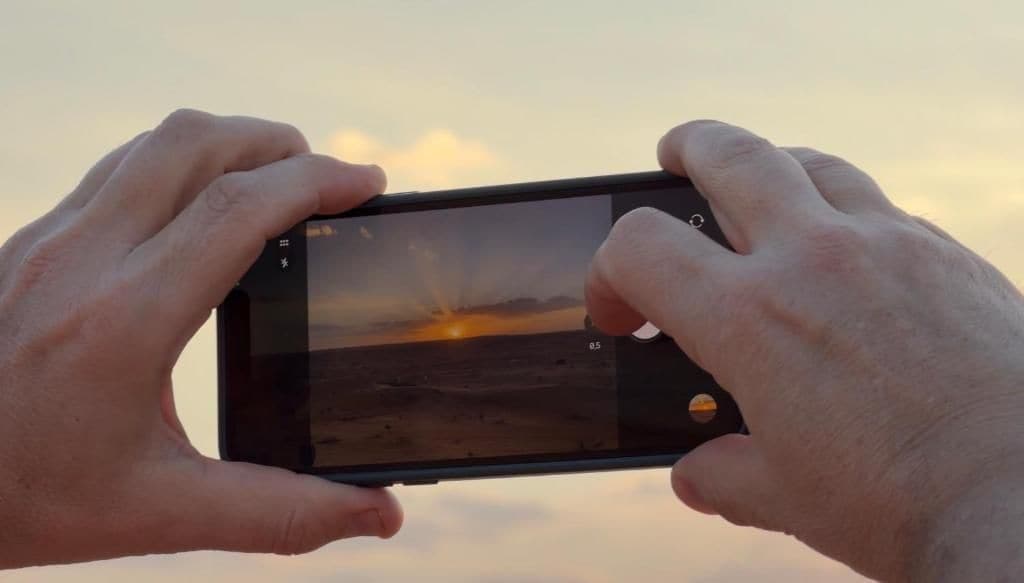 A person holding a smartphone, capturing a sunset view.