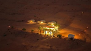 Paisaje desértico con varios edificios, algunos con ventanas iluminadas, que sugiere un entorno de resort o hotel.