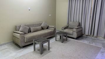 Un salon comprenant un canapé, un fauteuil, deux tables d’appoint et un tapis à motifs.