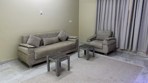 Una sala de estar con un sofá, un sillón, dos mesitas auxiliares y una alfombra estampada.
