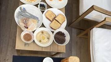 A breakfast setup with various food items and beverages on a table, a yoga mat, and a bed with white sheets.