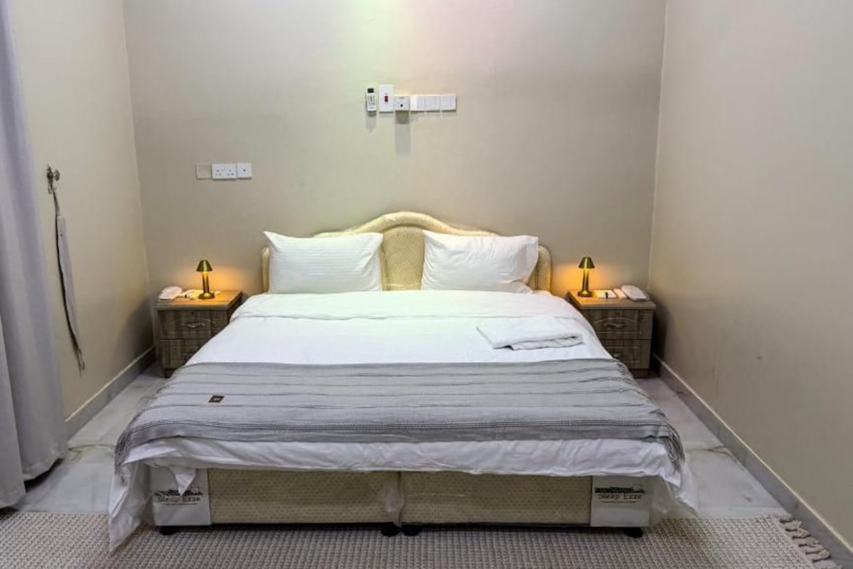 Ein Hotelzimmer mit einem Bett, Nachttischlampen, einem Telefon und einer Steckdose an der Wand.