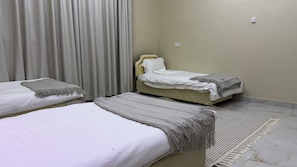 Ein Hotelzimmer mit zwei Einzelbetten, einem großen Fenster mit Vorhängen, einer schlichten Wand und einem gefliesten Boden.