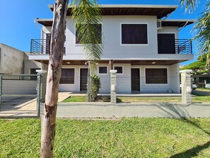 A two-story house with a balcony, a fenced yard, and a palm tree.