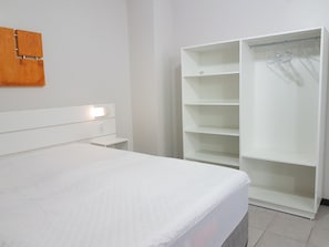 Een slaapkamer met een bed, een witte kledingkast met meerdere planken, en een wandlamp.