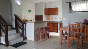 Een keuken met houten kastjes, een magnetron en een spoelbak. Er is een eethoek met een tafel en stoelen.