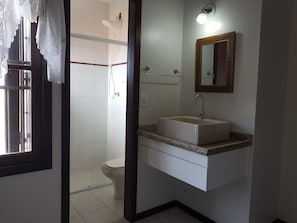 Een badkamer met douche, toilet, wastafel en spiegel.