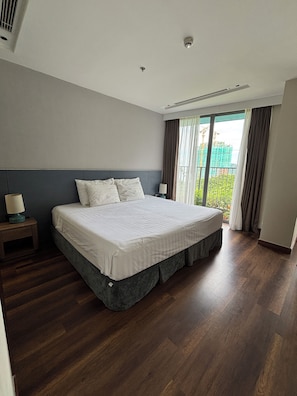 A hotel room with a large bed, a nightstand, a lamp, and a view of a construction site through the window. - Blue Sea & Sand Cat Ba Resort (Cat Ba Island)