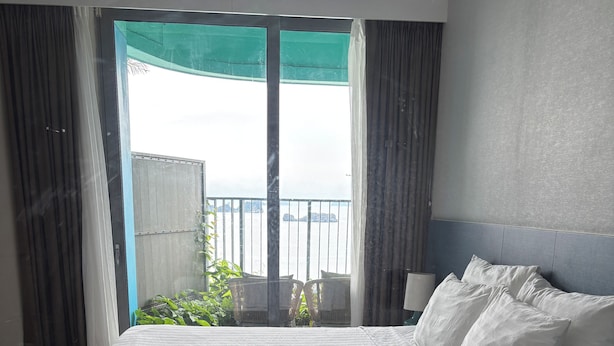 Een hotelkamer met een groot bed, uitzicht op zee via een balkon en een raam met gordijnen.