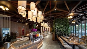 Een restaurantinterieur met een lange toonbank, hangende pendelverlichting en een groene wand.