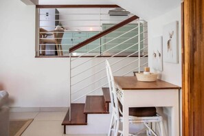 Eine Treppe mit hölzernem Geländer und weißen Spindeln, die zu einem Küchenbereich mit einem hellblauen Schrank und einem Stuhl führt.