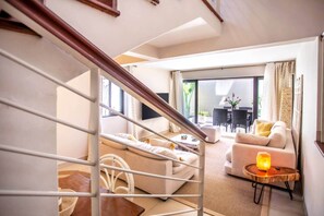 Un salon moderne avec un escalier, un ensemble de canapés, un coin repas et une vue sur l’extérieur.