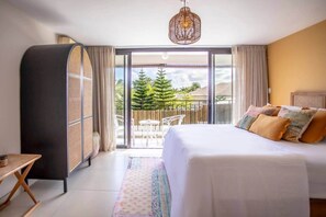 Une chambre d’hôtel avec un lit, un balcon donnant sur la verdure et un luminaire suspendu.