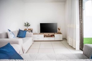 A modern living room with a flat-screen TV, a sofa, a coffee table, and a sliding glass door leading to a balcony. - Stylish Central Three Bed Duplex with Private Pool (Flic en Flac)