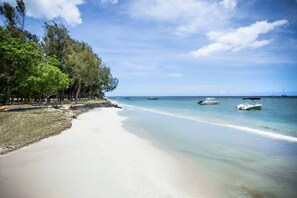 A beach with clear water, boats, and trees. - Cosy Bungalow with Pool and Beach Access (Black River)