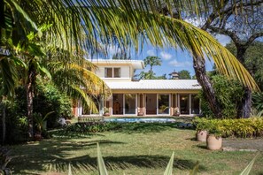 A two-story house with a covered patio, surrounded by lush greenery and a swimming pool. - Cosy Bungalow with Pool and Beach Access (Black River)