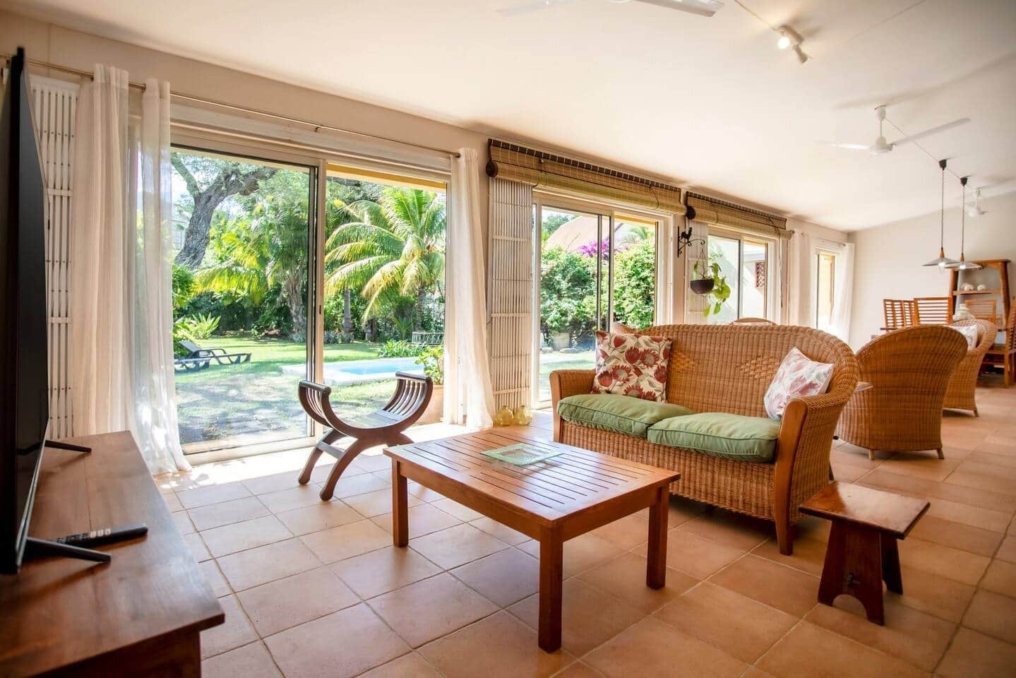 A spacious living area with a sofa, a coffee table, and a TV. Large windows provide a view of the outdoors.