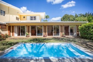A two-story house with a swimming pool, large sliding glass doors, and a well-maintained lawn. - Cosy Bungalow with Pool and Beach Access (Black River)