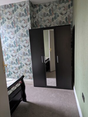Une chambre à coucher avec une armoire à deux portes, un lit et un papier peint à motifs.