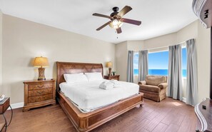 A spacious bedroom with a large bed, a ceiling fan, a view of the ocean, and a chaise lounge. - Tidewater 1605- Sunset Dreams (Panama City Beach)