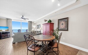 A dining area with a round table and chairs, a ceiling fan, and a view of the ocean through large windows. - Tidewater 1605- Sunset Dreams (Panama City Beach)