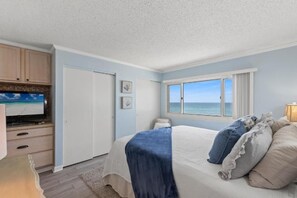 A bedroom with a bed, a television, a window with a view of the ocean, and a door. - Pinnacle Port C1-403 (Panama City Beach)