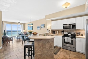 A modern kitchen with white cabinets, a large island, stainless steel appliances, and a view to the outside. - Celadon 408 (Panama City Beach)