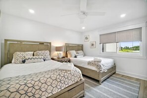 Ein Hotelzimmer mit zwei Betten, einem Deckenventilator, einem Fenster mit Blick und einem kleinen Tisch mit Lampe.