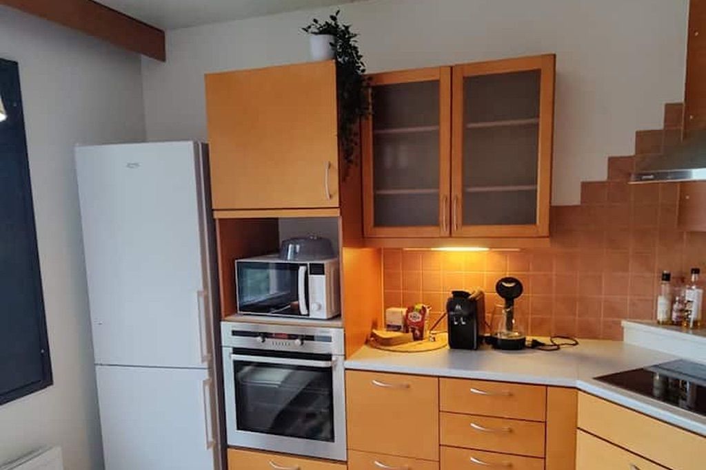 Een kleine keuken met een koelkast, oven, magnetron en koffiezetapparaat op het aanrecht.