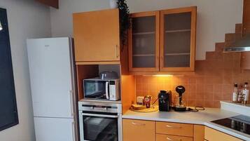 Een kleine keuken met een koelkast, oven, magnetron en koffiezetapparaat op het aanrecht.