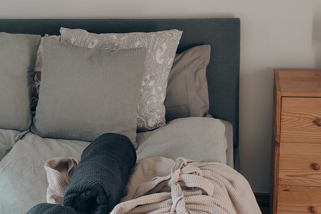 A bed with a grey headboard, multiple pillows, and a wooden nightstand beside it.