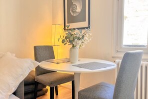 Une petite table de salle à manger ronde, accompagnée de deux chaises, un vase avec des fleurs et un tableau encadré accroché au mur.