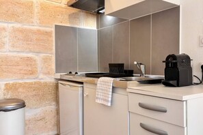Une cuisine compacte équipée d’une cuisinière intégrée, d’une machine à café et d’un égouttoir à vaisselle.